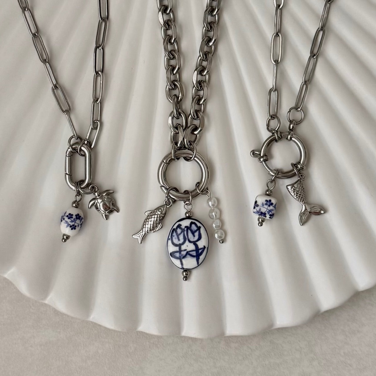 Three silver necklaces with various charms on a white shell background