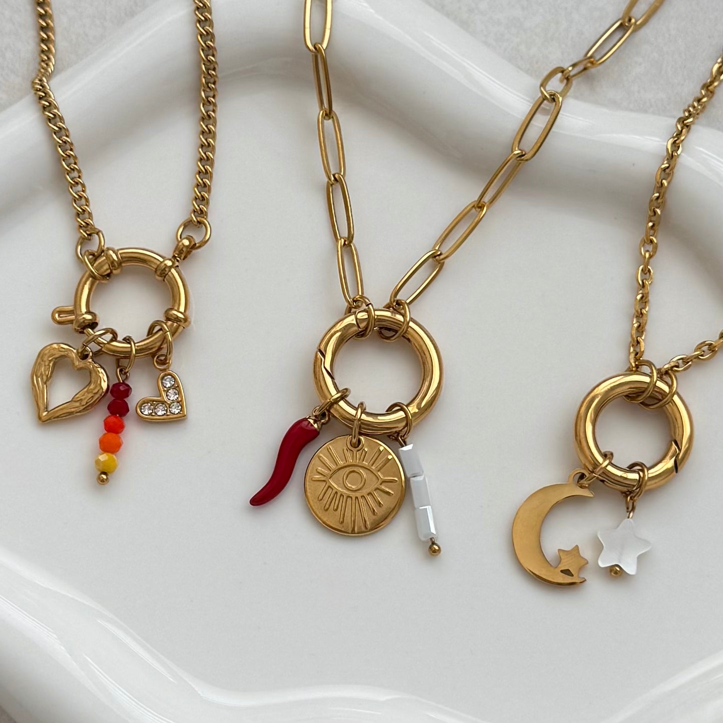 Three gold necklaces with various charms on a white surface