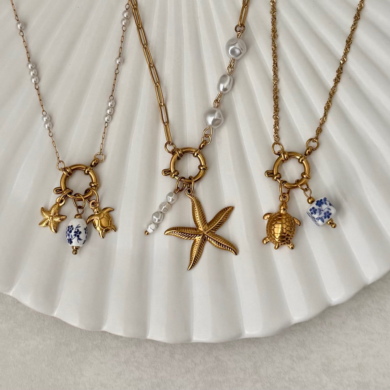 Three gold necklaces with starfish and turtle charms on a white shell background