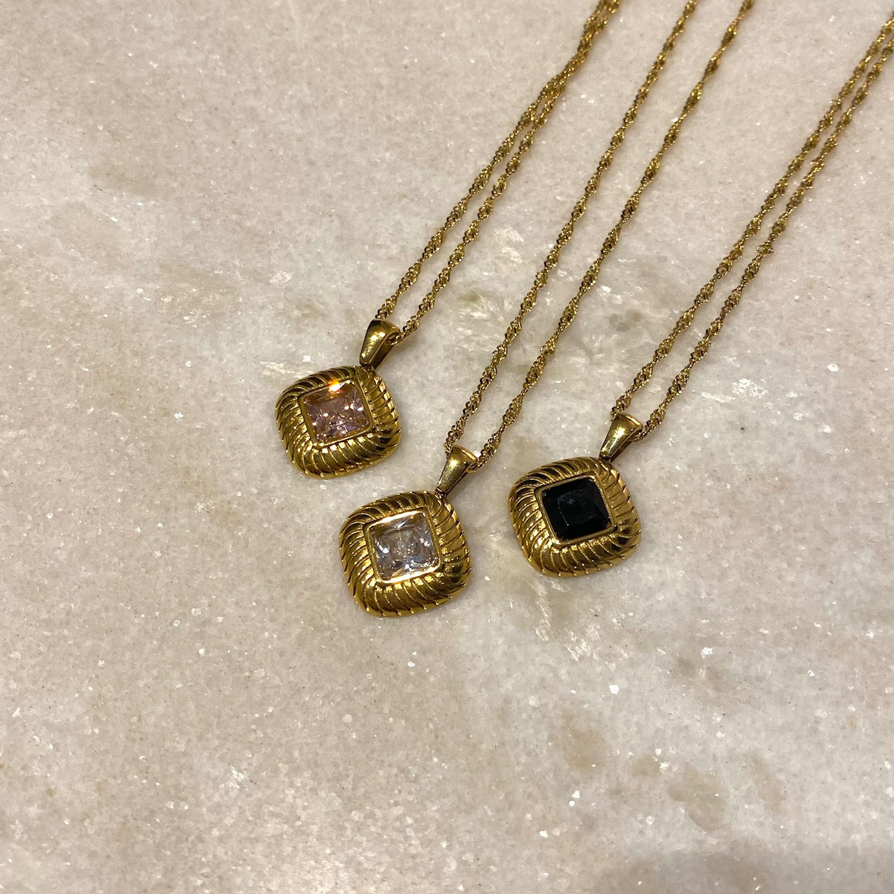 three gold pendants, clear black and pink zircon