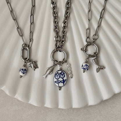 Three silver necklaces with various charms on a white shell background
