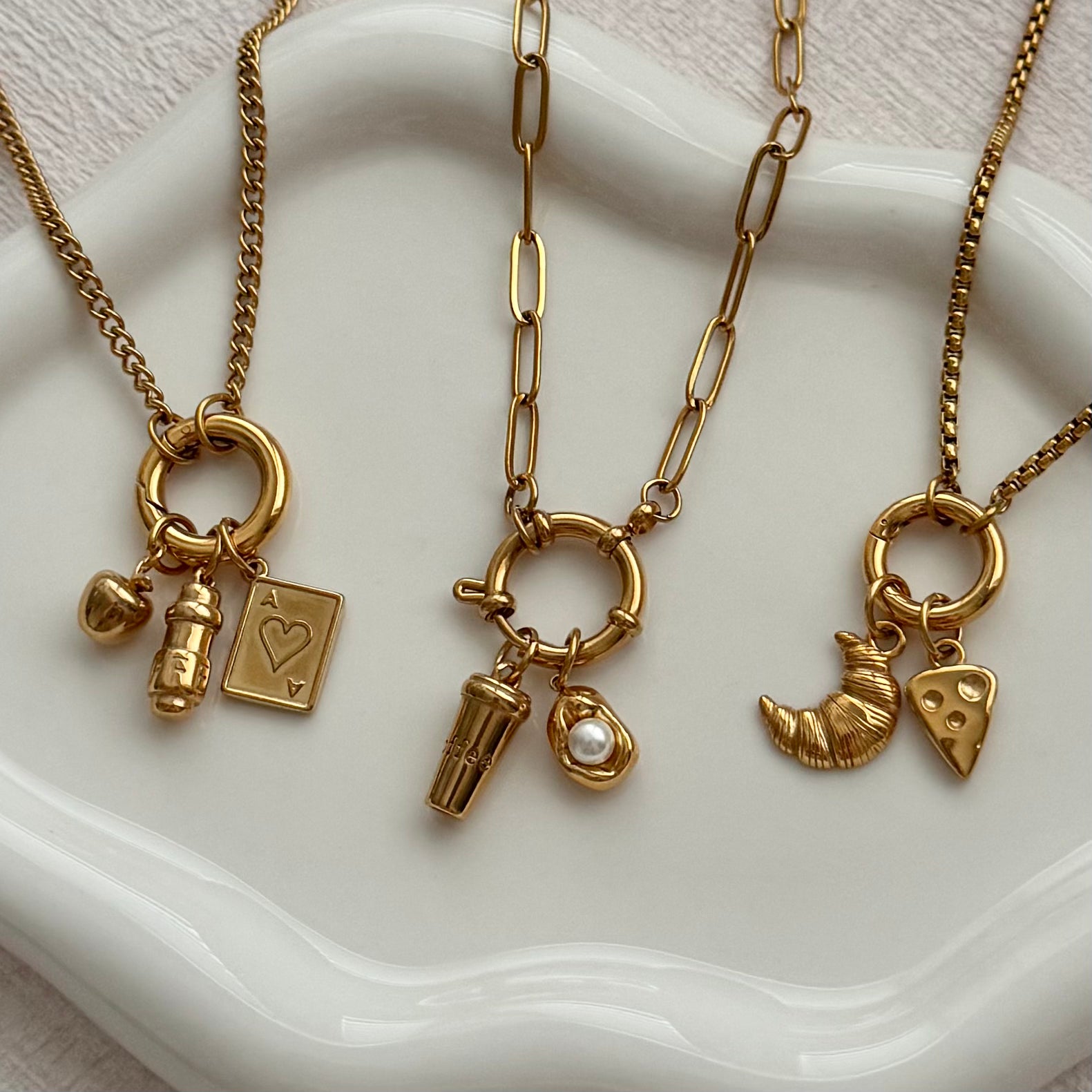 Three gold necklaces with various charms on a white dish.