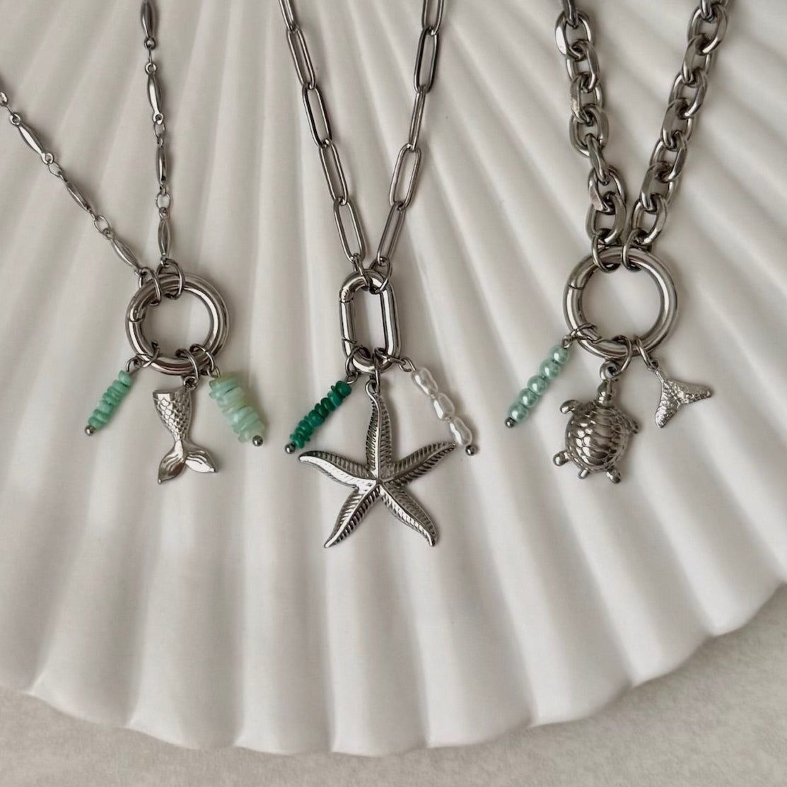 Three silver necklaces with charms on a shell background