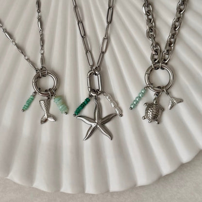 Three silver necklaces with charms on a shell background